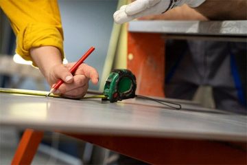 A worker that shows how to measure a dining table with a roulette and a pencil