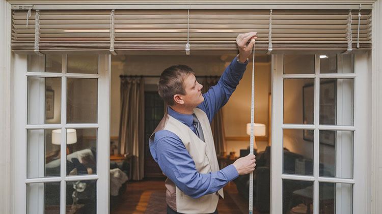 A man is measuring for window blinds in his house